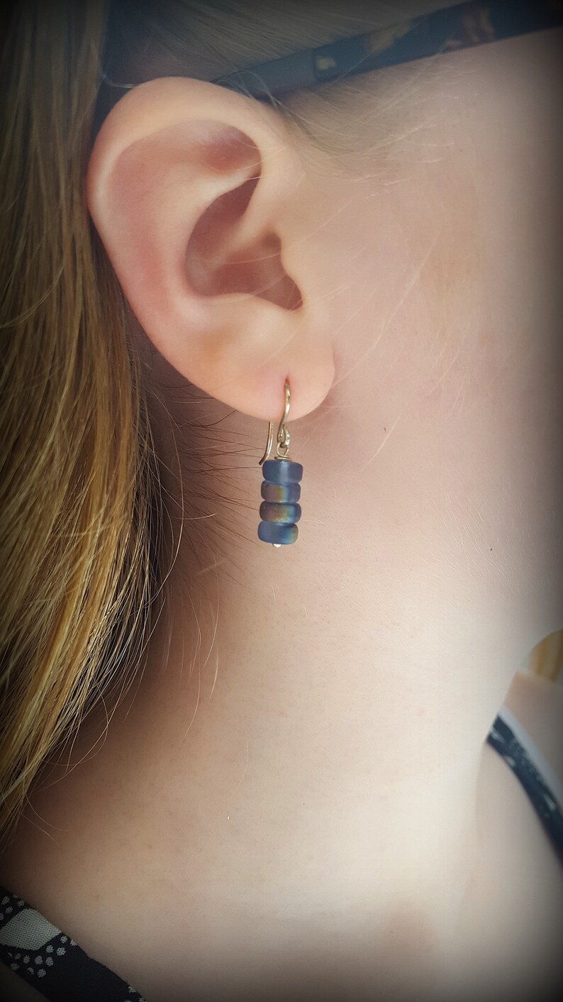 May include: A pair of earrings with a gold hook and a stack of iridescent blue glass beads.