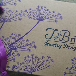 May include: A brown cardboard box with a purple floral design and the text "T and Brie Jewelry Design".
