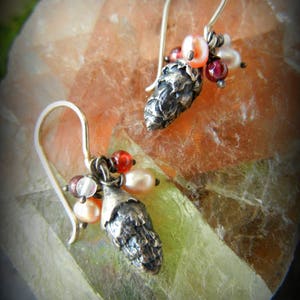 May include: A pair of silver earrings with a pine cone charm and a cluster of red, pink, and white beads.