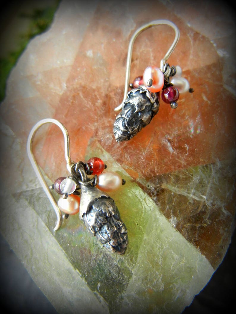 May include: A pair of silver earrings with a pine cone charm and a cluster of red, pink, and white beads.