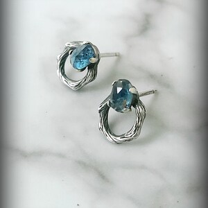 Peut inclure: Une paire de boucles d'oreilles en argent avec une pierre pr&eacute;cieuse bleue sertie dans un design de fil torsad&eacute;.