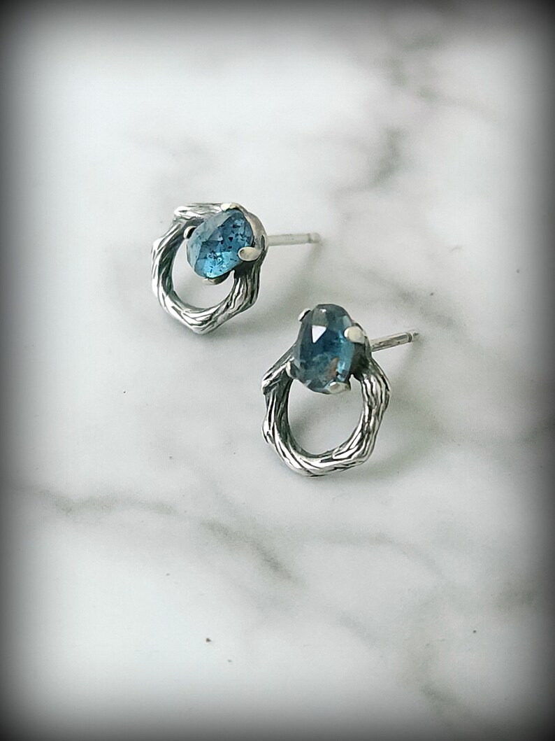 Peut inclure: Une paire de boucles d'oreilles en argent avec une pierre pr&eacute;cieuse bleue sertie dans un design de fil torsad&eacute;.