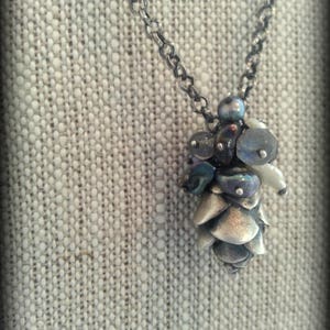 May include: A silver chain necklace with a silver and iridescent glass pine cone pendant.
