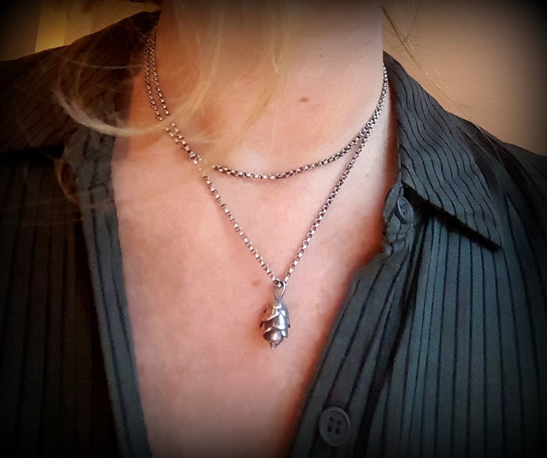 May include: A silver chain necklace with a silver pendant shaped like a pine cone.