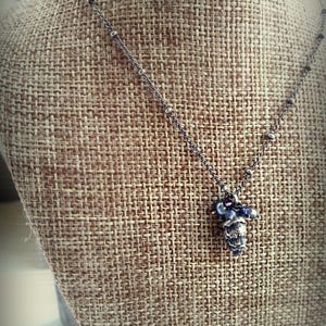 May include: A silver chain necklace with a small, detailed pinecone charm and purple beads.