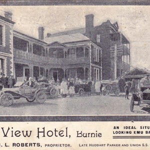 May include: Vintage black and white advertisement for the Bay View Hotel in Burnie, Tasmania. The image shows the hotel building, cars, and people. Text includes the hotel name, location, and proprietor's name.