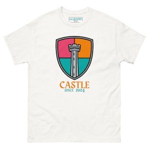 May include: White t-shirt with a colorful graphic of a castle tower inside a shield. The shield has pink, orange, and teal sections. The word "CASTLE" and the year "SINCE 2024" are printed below the shield. The shirt also has the text "sa.GRAPHIX design" on the upper part.