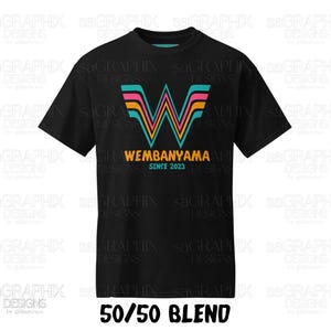 Pu&ograve; includere: Una t-shirt nera a maniche corte con una grande lettera W stilizzata a strisce turchesi, rosa e arancioni. Sotto la lettera, il testo recita WEMBANYAMA in arancione e SINCE 2023 in turchese. In basso &egrave; riportato il testo 50/50 BLEND.