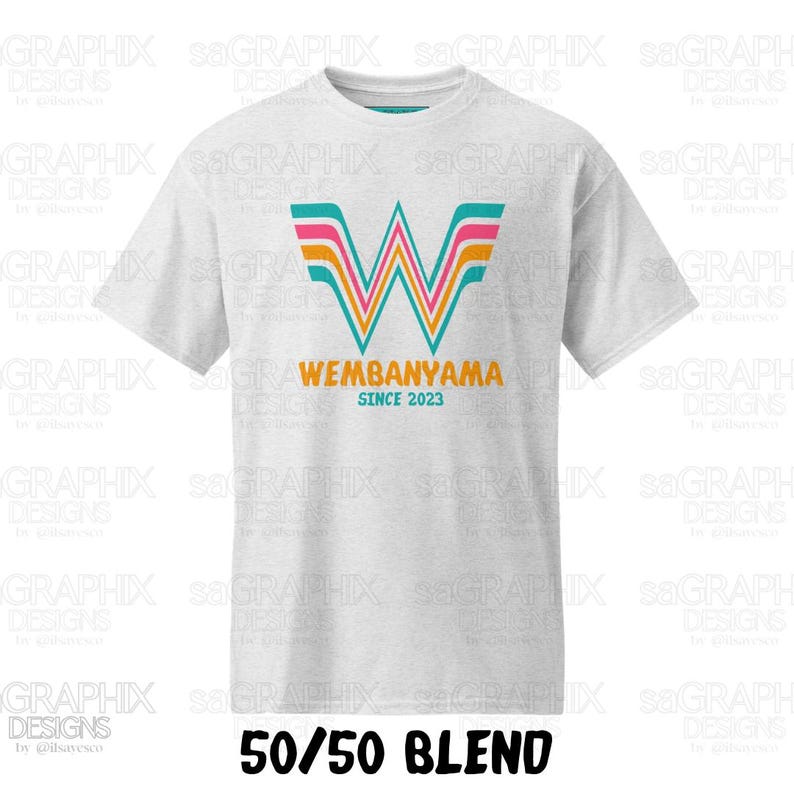 Pu&ograve; includere: Una t-shirt grigio chiaro a maniche corte con una grande lettera W stilizzata a strisce color turchese, rosa e arancione. Sotto la grafica, il testo recita WEMBANYAMA in arancione e SINCE 2023 in turchese. Il testo in basso indica 50/50 BLEND.