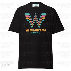 May include: Black t-shirt featuring a colorful "W" graphic with pink, teal, and yellow stripes, above the word "WEMBANYAMA" in yellow, and "SINCE 2023" below. A casual tee for everyday wear.