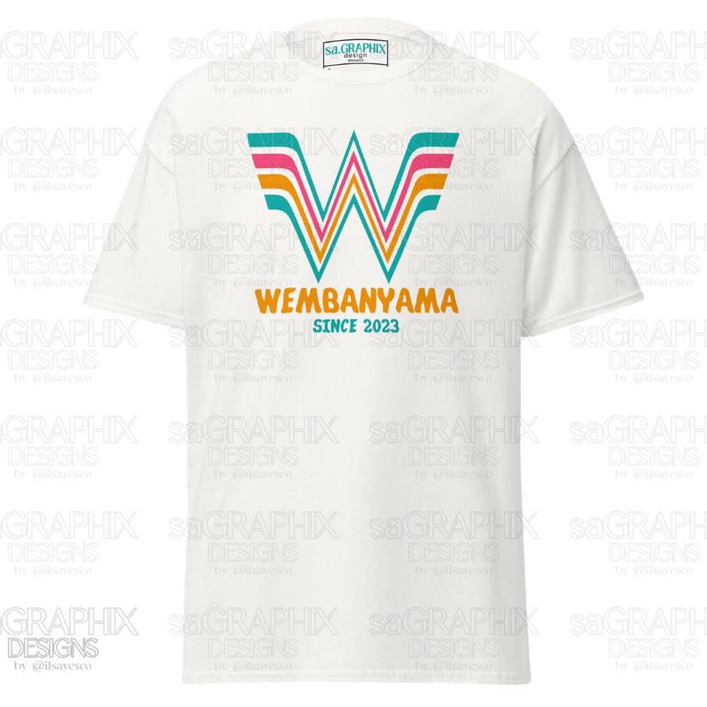 May include: White t-shirt featuring a colorful graphic design. The design includes a stylized "W" with pink, orange, and teal accents, along with the text "WEMBANYAMA SINCE 2023" in orange. The shirt has a classic crew neck.