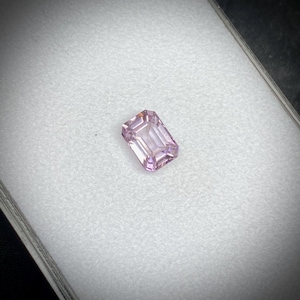 Peut inclure: Une pierre précieuse rectangulaire rose clair, taillée en émeraude. La gemme est posée sur un fond blanc, avec un léger effet d'ombre. Les facettes de la pierre reflètent la lumière, mettant en valeur sa clarté et sa couleur.