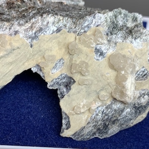 May include: A close-up of a rock formation with a layered appearance. The rock has a mix of grey and silver tones, with a lighter, beige-coloured section on top. Small, rounded, light-coloured formations are visible on the beige section.