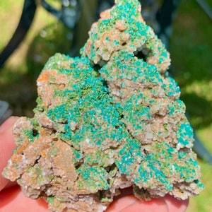 Puede incluir: Primer plano de un espécimen mineral con una mezcla de colores y texturas. La roca tiene una base marrón claro con parches blancos y está cubierta de vibrantes cristales verde turquesa. La apariencia general es áspera y natural.