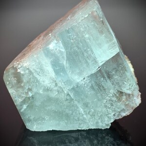 Puede incluir: Un gran cristal de aguamarina transl&uacute;cido con forma rectangular. El cristal tiene un tono azul verdoso p&aacute;lido y una superficie rugosa y texturizada. Los bordes son afilados y bien definidos, y el cristal parece estar parcialmente pulido.