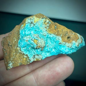 May include: A rough-hewn rock sample featuring a vibrant turquoise mineral formation. The turquoise contrasts with the surrounding earthy brown and yellow tones of the rock. The mineral appears crystalline and textured.