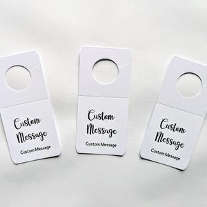May include: Three white hang tags with a hole at the top. Each tag has the text "Custom Message" printed on it.