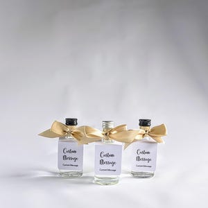 May include: Three small glass bottles with gold ribbon bows and white labels that say "Custom Message".