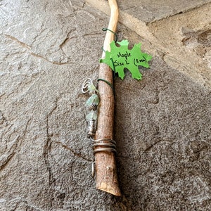 May include: A wooden wand with a green leaf tag that says "Maple Size L (8 mm)". The wand is decorated with silver wire and green stones.