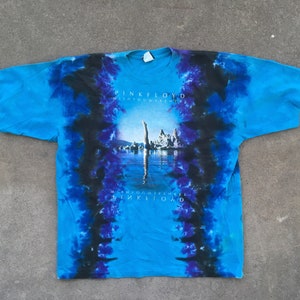 Może przedstawiać: Niebieska koszulka tie-dye z czarnym i fioletowym wzorem. Koszulka przedstawia grafikę osoby nurkującej w wodzie z nadrukiem "Pink Floyd Wish You Were Here" na przodzie.