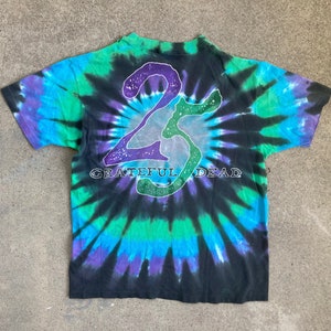 Puede incluir: Una camiseta negra tie-dye con un gr&aacute;fico "25" blanco y morado y el texto "Grateful Dead" en blanco.