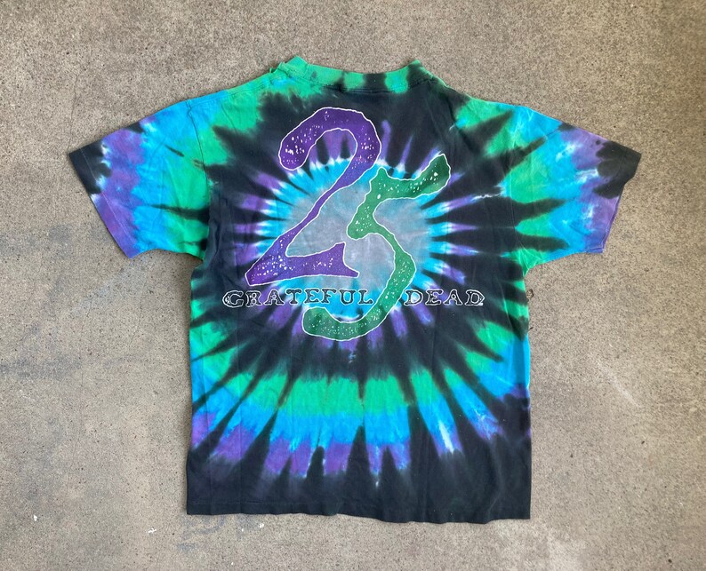 Puede incluir: Una camiseta negra tie-dye con un gr&aacute;fico "25" blanco y morado y el texto "Grateful Dead" en blanco.