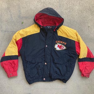 May include: A black, red, and yellow hooded jacket with the word "CHIEFS" and a team logo on the chest. The jacket has a red interior lining, two front pockets, and a button-up closure. The sleeves are red, yellow, and black.