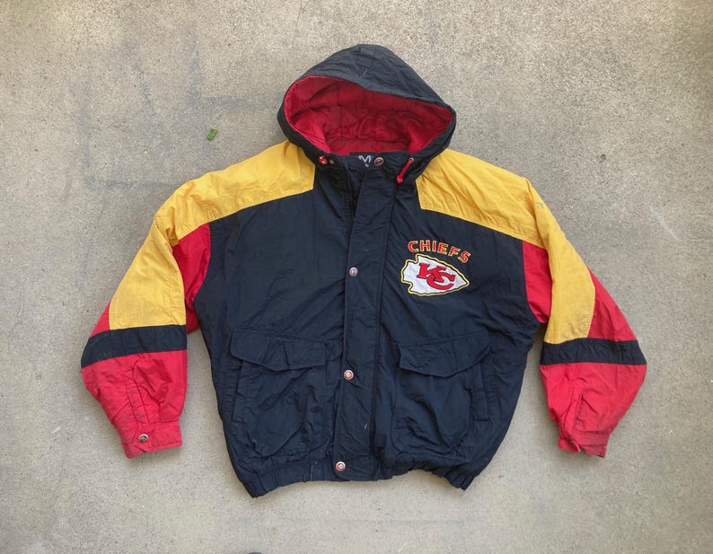 May include: A black, red, and yellow hooded jacket with the word "CHIEFS" and a team logo on the chest. The jacket has a red interior lining, two front pockets, and a button-up closure. The sleeves are red, yellow, and black.