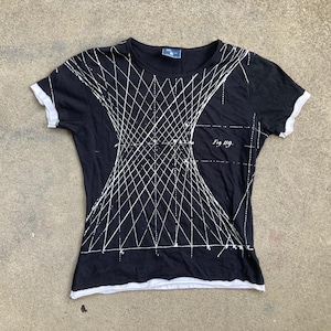 Puede incluir: Camiseta negra con dise&ntilde;o geom&eacute;trico blanco. La camiseta de manga corta tiene ribetes blancos en las mangas y el cuello. El texto "Fig. 119" est&aacute; impreso en la parte delantera.