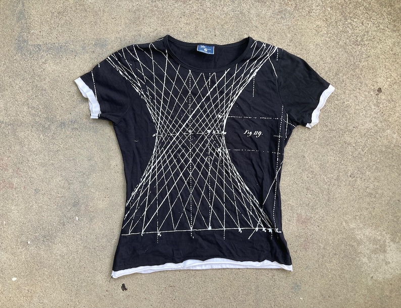 Puede incluir: Camiseta negra con dise&ntilde;o geom&eacute;trico blanco. La camiseta de manga corta tiene ribetes blancos en las mangas y el cuello. El texto "Fig. 119" est&aacute; impreso en la parte delantera.