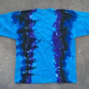 Może przedstawiać: Niebieska koszulka tie-dye z czarnymi i fioletowymi smugami barwnika. Koszulka ma luźny kr&oacute;j i okrągły dekolt.