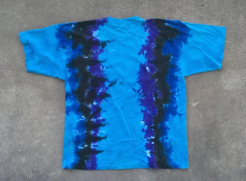 Może przedstawiać: Niebieska koszulka tie-dye z czarnymi i fioletowymi smugami barwnika. Koszulka ma luźny kr&oacute;j i okrągły dekolt.