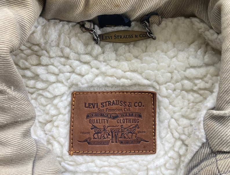 Puede incluir: Un parche de cuero marr&oacute;n Levi Strauss & Co. con el texto "Levi Strauss & Co. San Francisco, Cal. Original Riveted Quality Clothing Trade Mark" en letras blancas.