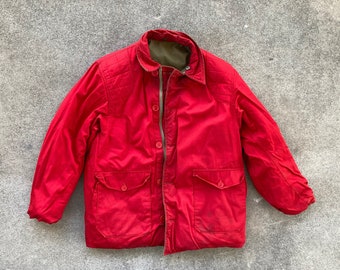 May include: A red quilted jacket with a zip closure and multiple pockets. The jacket has a brown lining and a quilted design on the shoulders.