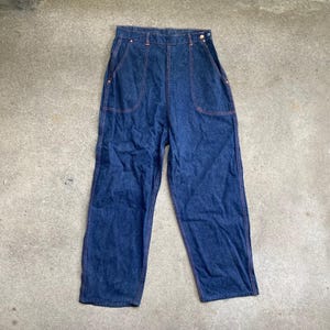 May include: Dark blue denim pants with orange stitching. The pants have a high waist, two front pockets, and a button closure. The denim is a medium weight, and the pants have a relaxed fit.