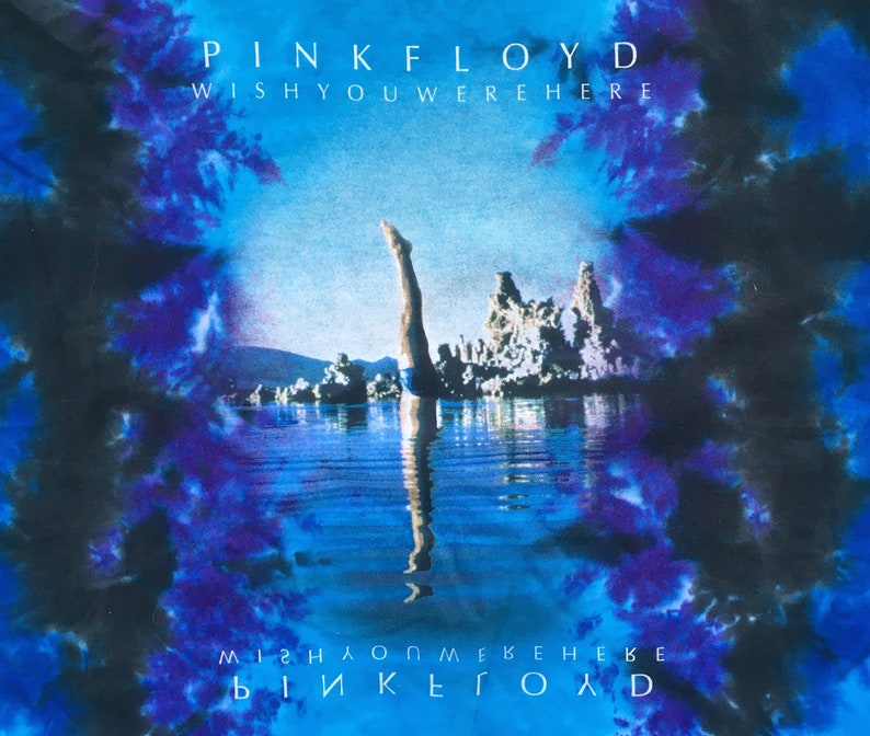 Może przedstawiać: Koszulka tie-dye z niebieskim i czarnym tłem. Prz&oacute;d koszulki przedstawia okładkę albumu "Wish You Were Here" zespołu Pink Floyd. Okładka albumu przedstawia mężczyznę nurkującego w zbiorniku wodnym z skalistym krajobrazem w tle. Tekst "Pink Floyd" i "Wish You Were Here" jest nadrukowany na koszulce na biało.