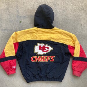 May include: A vintage Kansas City Chiefs hooded jacket. The jacket features a black hood and a color block design with yellow, red, and navy blue panels. The Chiefs logo and team name are prominently displayed on the back.