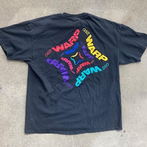 Pode incluir: Camiseta preta com um design de logotipo "WARP" colorido nas costas. O logotipo é um design circular com a palavra "WARP" repetida várias vezes em diferentes cores.