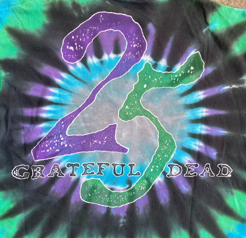 Puede incluir: Una camiseta negra tie-dye con un contorno blanco del n&uacute;mero 23 y las palabras "Grateful Dead" en blanco.