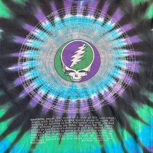 Puede incluir: Una camiseta tie-dye negra, azul y verde con un gr&aacute;fico circular de una calavera con un rayo y el texto "Grateful Dead". El texto "Winter 95 Tage" tambi&eacute;n es visible en la camiseta.