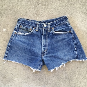 Puede incluir: Un par de pantalones cortos de mezclilla azul con bordes deshilachados. Los pantalones cortos tienen cintura alta y cinco bolsillos.