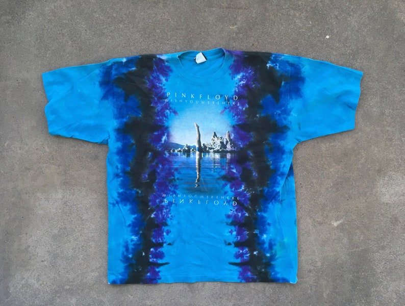 Może przedstawiać: Niebieska koszulka tie-dye z czarnym i fioletowym wzorem. Koszulka przedstawia grafikę osoby nurkującej w wodzie z nadrukiem "Pink Floyd Wish You Were Here" na przodzie.