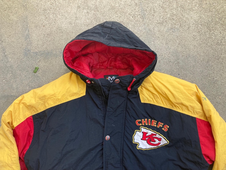 May include: A hooded jacket with a black body, yellow shoulders, and red accents. The jacket features the Kansas City Chiefs logo and the word "CHIEFS" in red and white.
