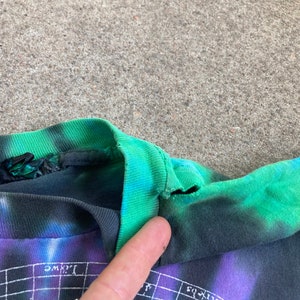 Puede incluir: Primer plano del cuello de una camiseta tie-dye con un esquema de color negro y verde. La camiseta tiene un peque&ntilde;o desgarro cerca del escote.