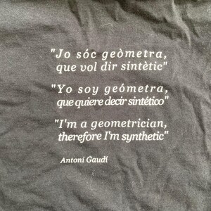 Puede incluir: Camiseta negra con texto blanco en tres idiomas: catal&aacute;n, espa&ntilde;ol e ingl&eacute;s. La cita, atribuida a Antoni Gaud&iacute;, dice: &laquo;Soy ge&oacute;metra, por lo tanto soy sint&eacute;tico&raquo;.