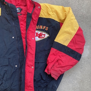 May include: A vintage black, red, and yellow jacket with a hood. The jacket features the word "CHIEFS" and a logo on the chest. The jacket has a zipper closure and two front pockets. The interior lining is red.