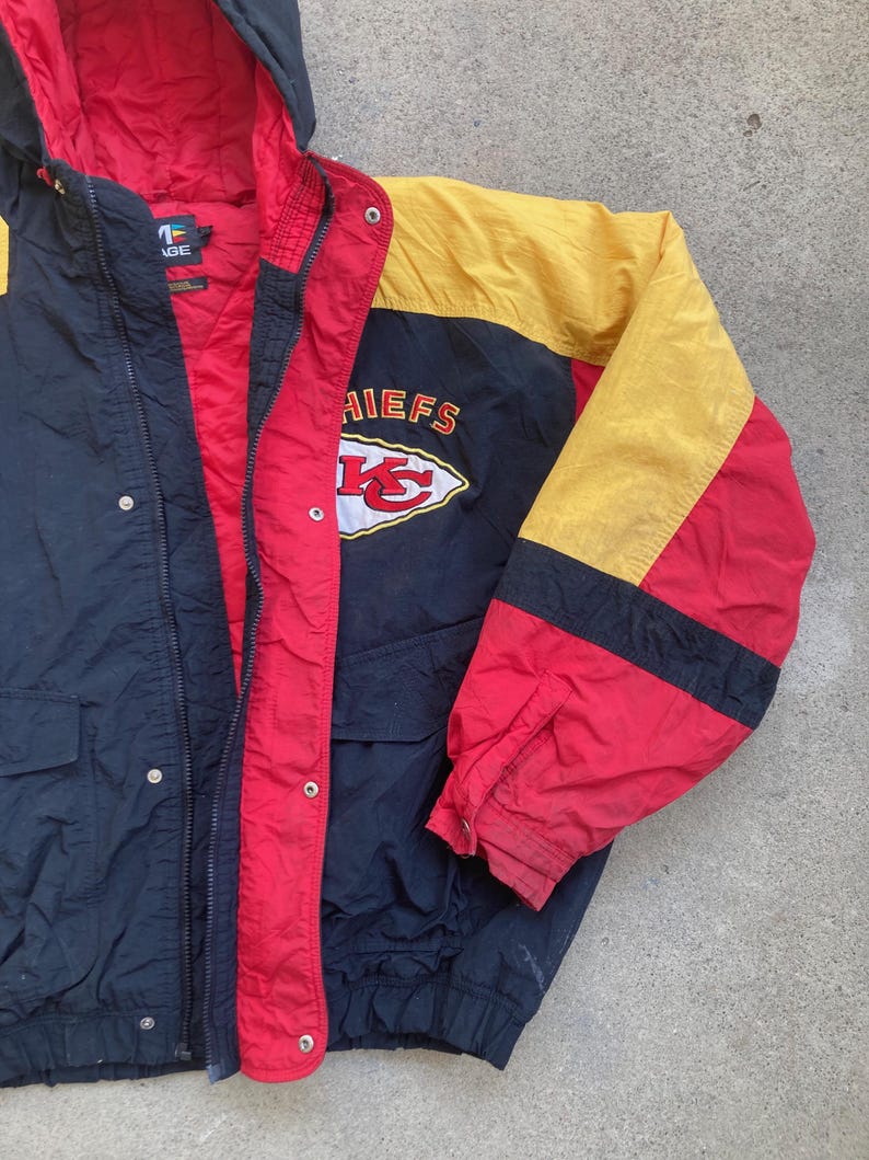 May include: A vintage black, red, and yellow jacket with a hood. The jacket features the word "CHIEFS" and a logo on the chest. The jacket has a zipper closure and two front pockets. The interior lining is red.