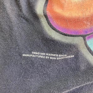 May include: Black t-shirt with a colourful graphic print. The text "TM&&copy;1995 Warner Bros. Manufactured by Sun Sportswear" is printed on the bottom of the shirt.