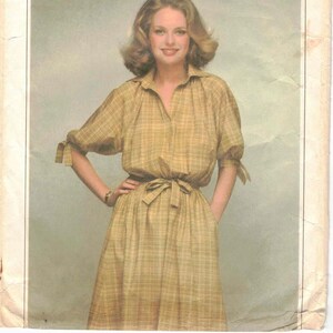 Puede incluir: Sobre de patrón de costura Simplicity vintage. El sobre presenta el texto "Simplicity ESP Extra-Sure Pattern" y una foto de una mujer con un vestido a cuadros. El vestido tiene una cintura anudada y mangas cortas con lazos.