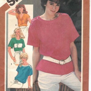 Pode incluir: Padrão de costura Simplicity número 5942 para uma blusa feminina. O padrão inclui quatro estilos diferentes de blusas, todas com mangas curtas. A modelo está usando uma blusa rosa com um cinto branco e calças brancas.